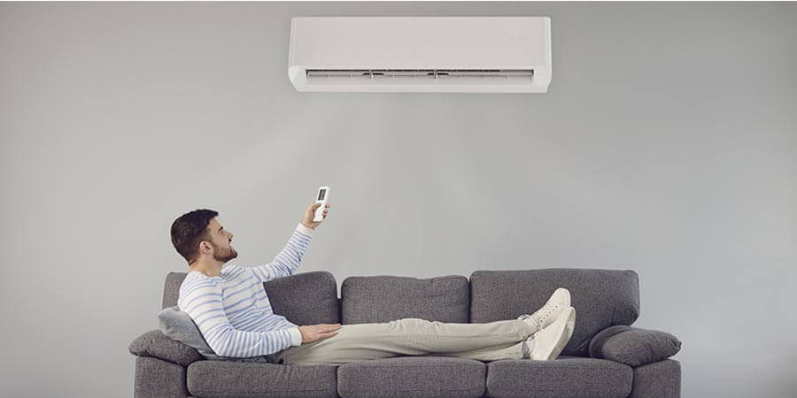 man lying on the couch turning on ductless unit